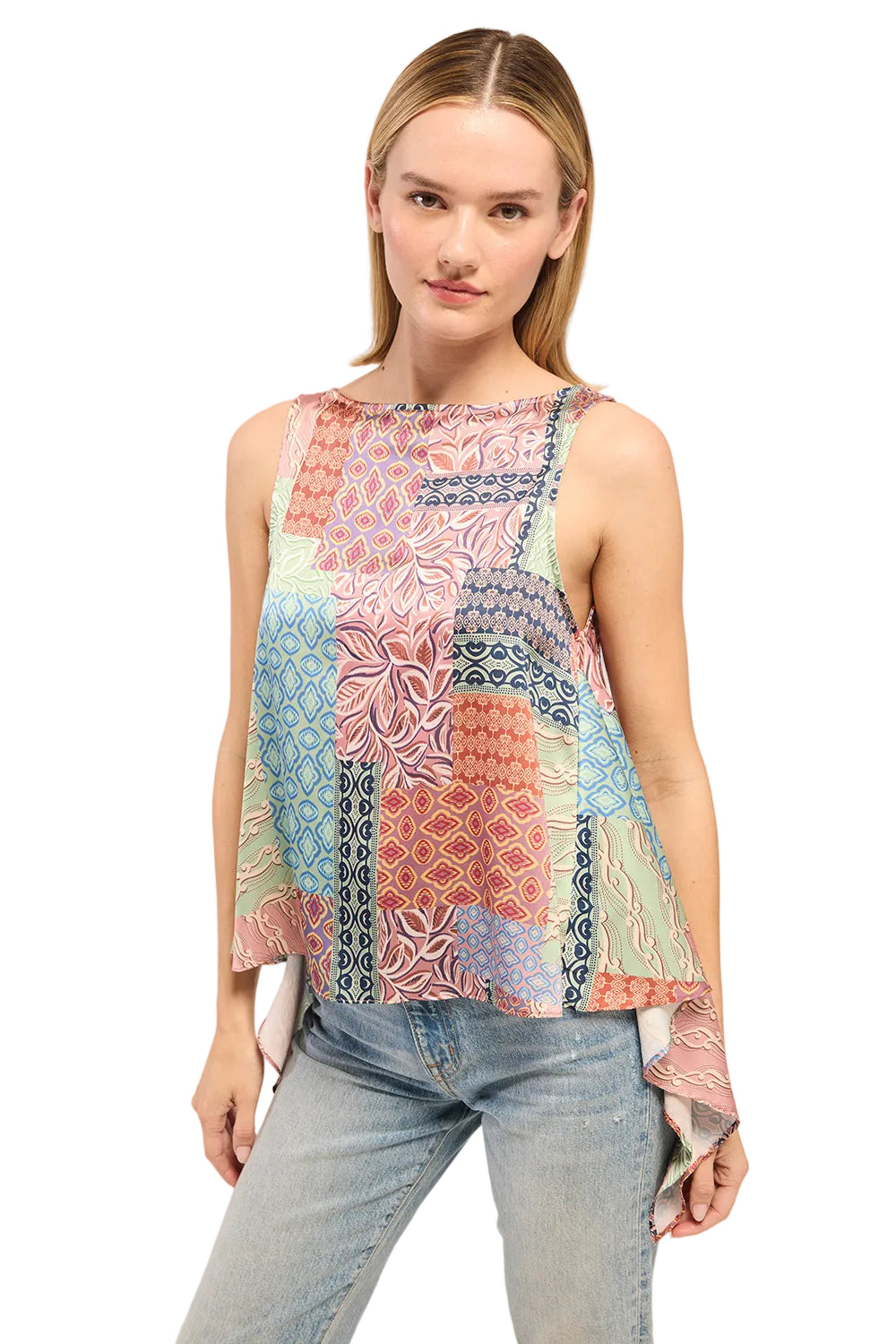 Woman wearing a colorful patterned sleeveless top and light blue jeans on a white background